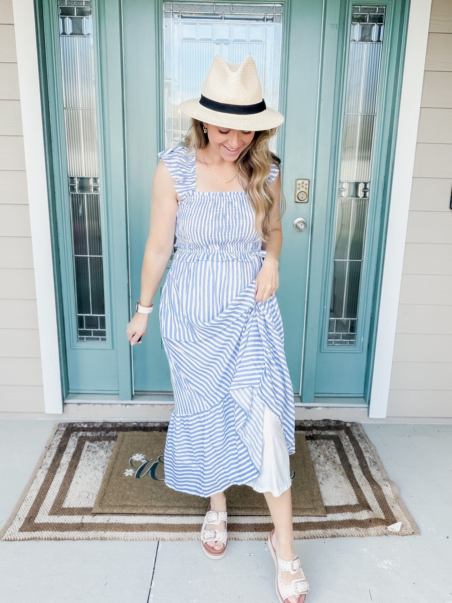 Woman in a blue and white striped dress standing in front of a teal door.