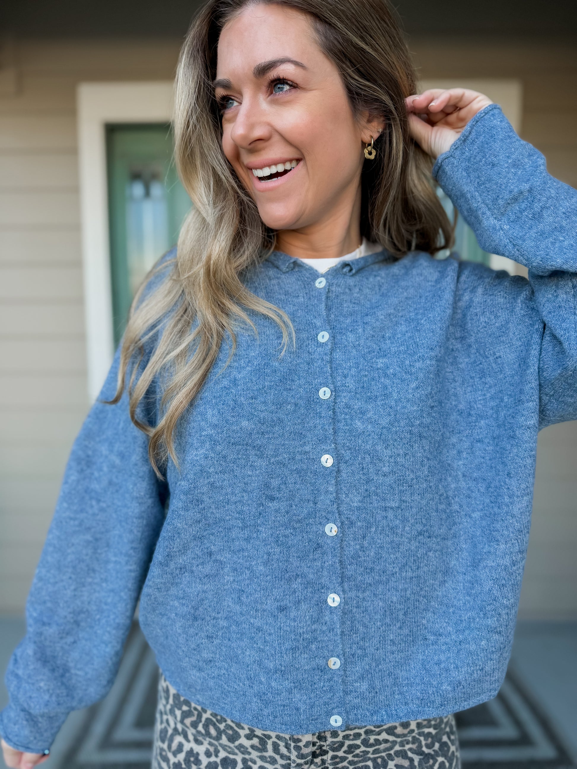 Woman wearing a blue cardigan with buttons with a neutral background. called cozy up everyday cardigan in dusty blue. 