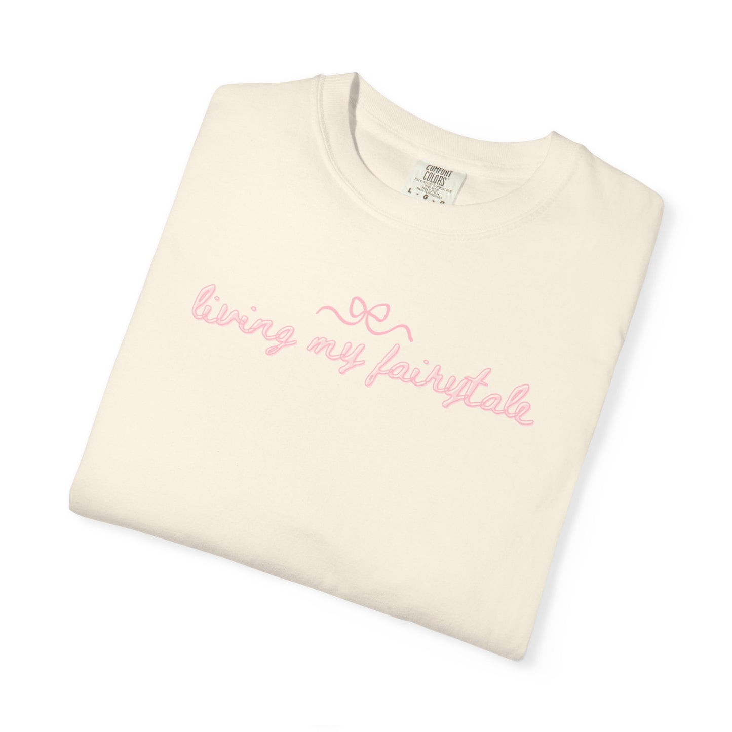 Folded cream-colored t-shirt with pink text "living my fairtyale" on a white background