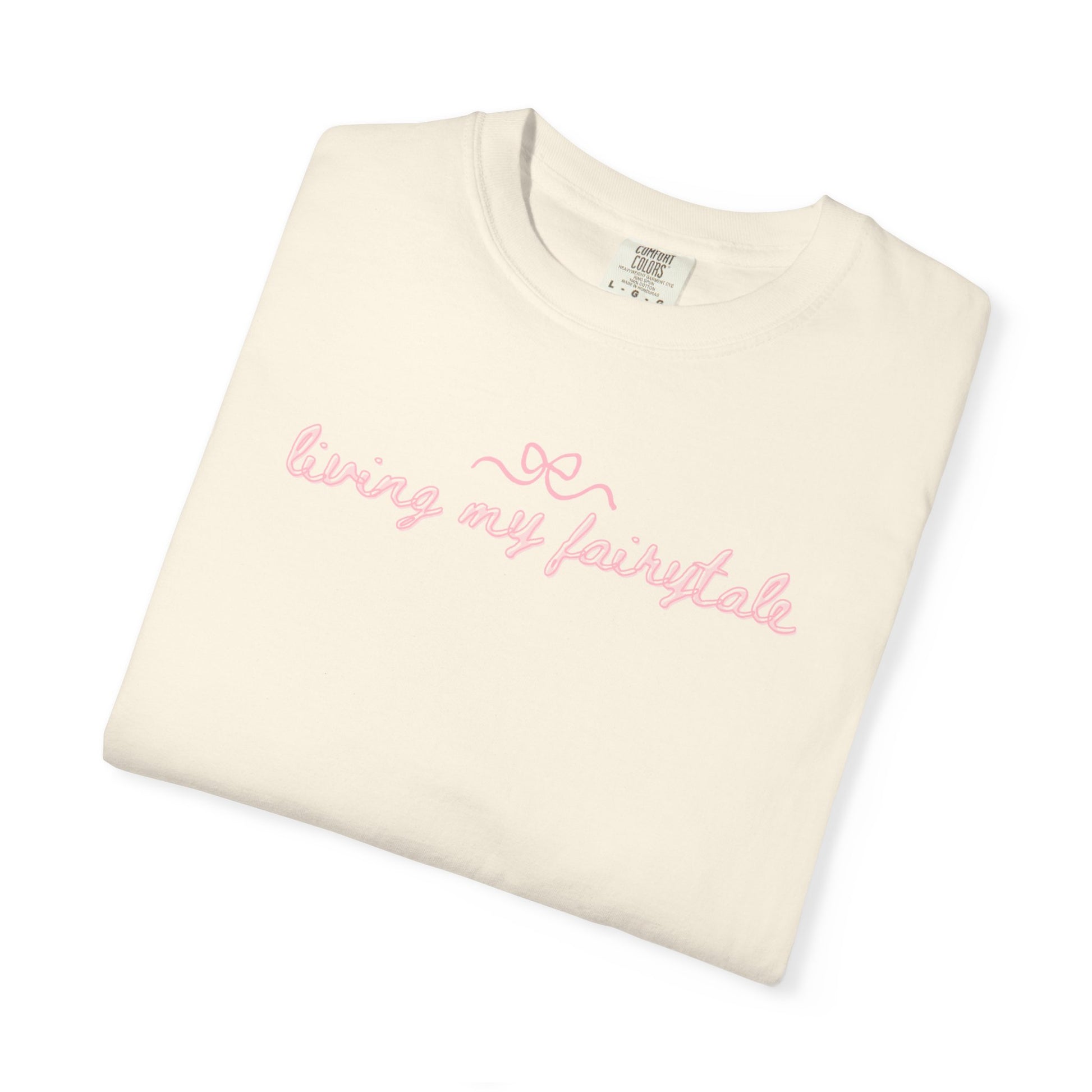 Folded cream-colored t-shirt with pink text "living my fairtyale" on a white background