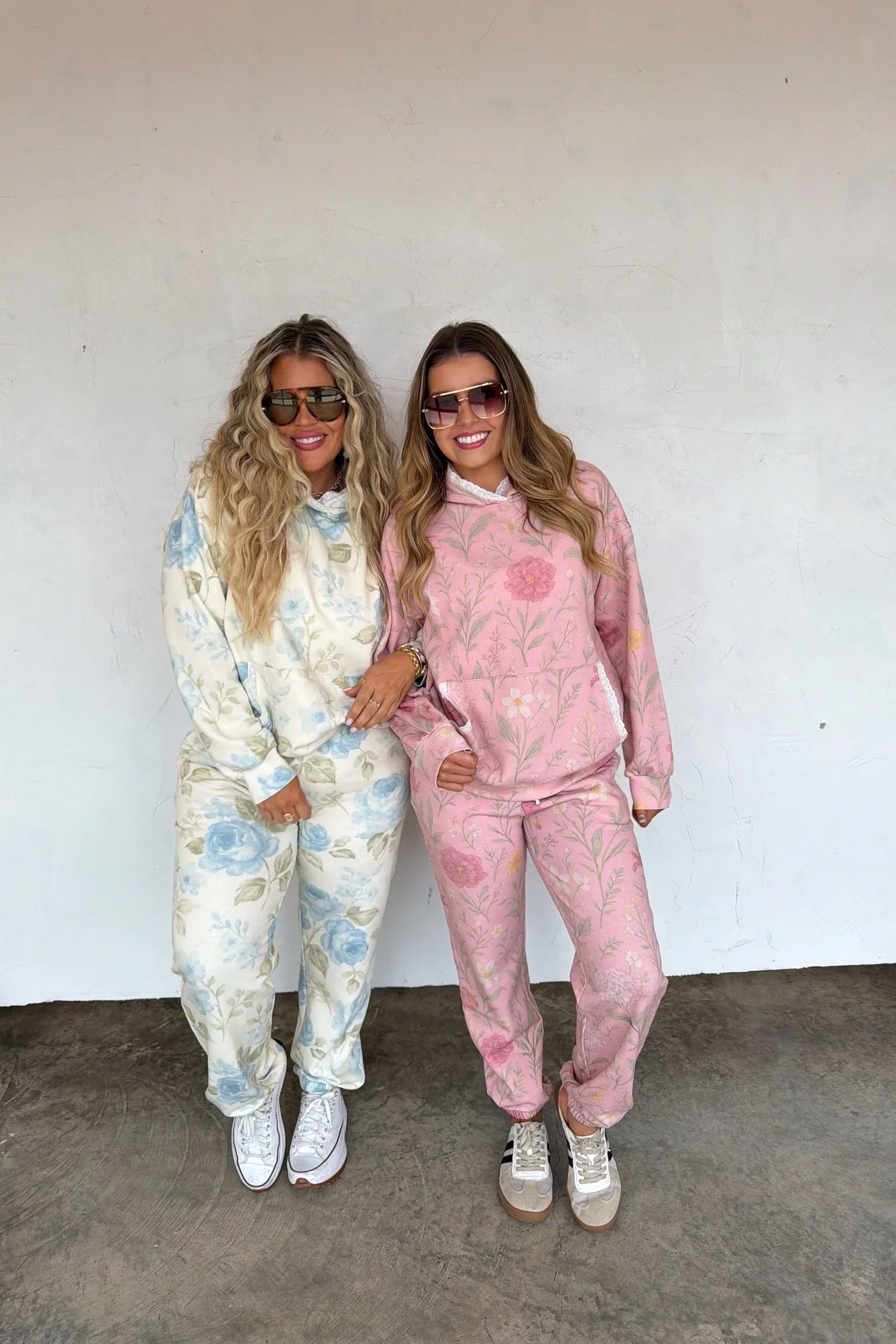 Two women posing together wearing matching floral jogger sets against a white wall.