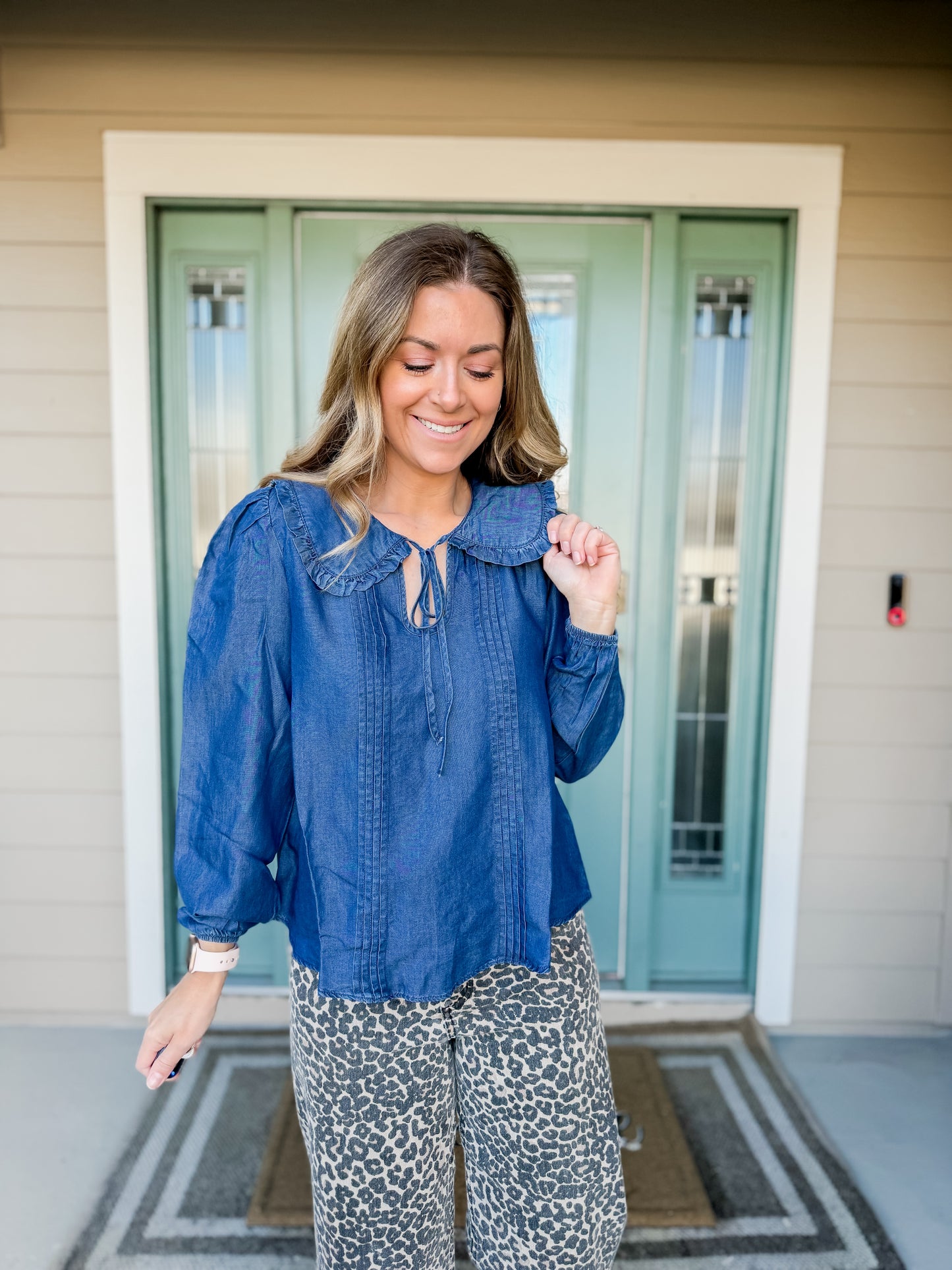 Woman wearing a blue blouse with collar and patterned pants standing in front of a door. called Cerulean collared blouse. 