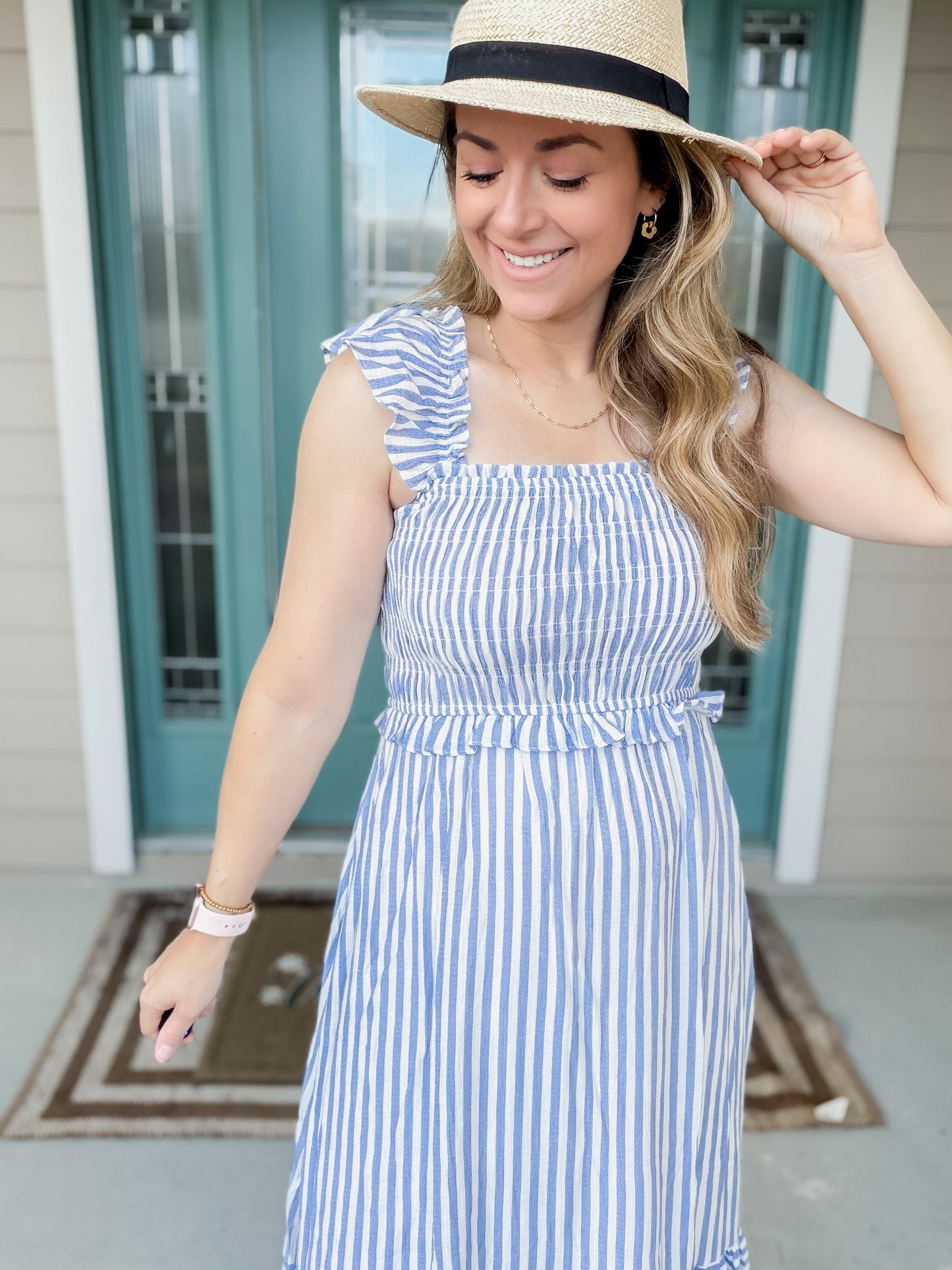 Woman wearing a blue and white striped dress and straw hat on a porch.