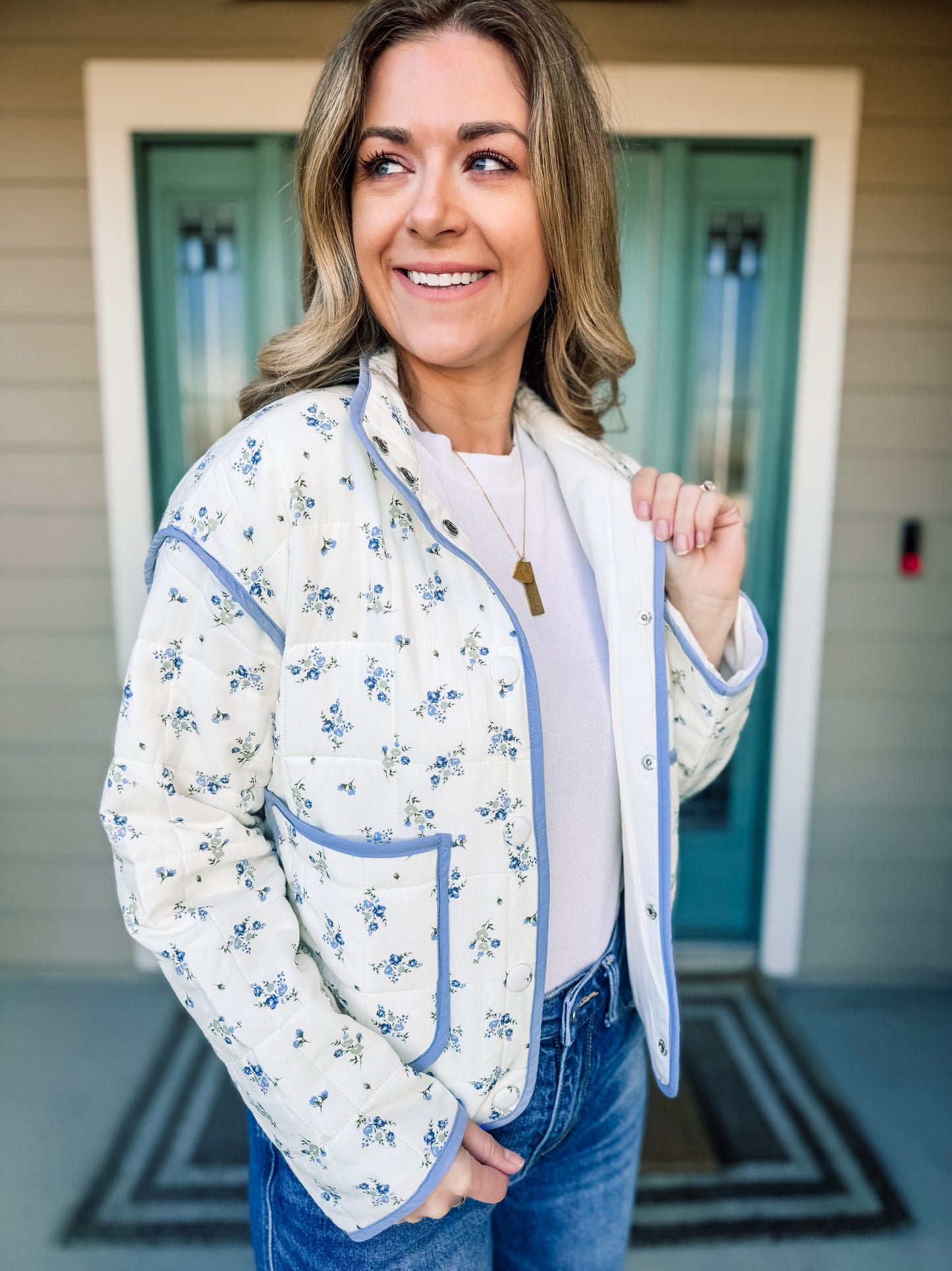 Woman wearing a floral quilted jacket with blue trim in front of a house entrance.Bloom in Blue Quilted Jacket