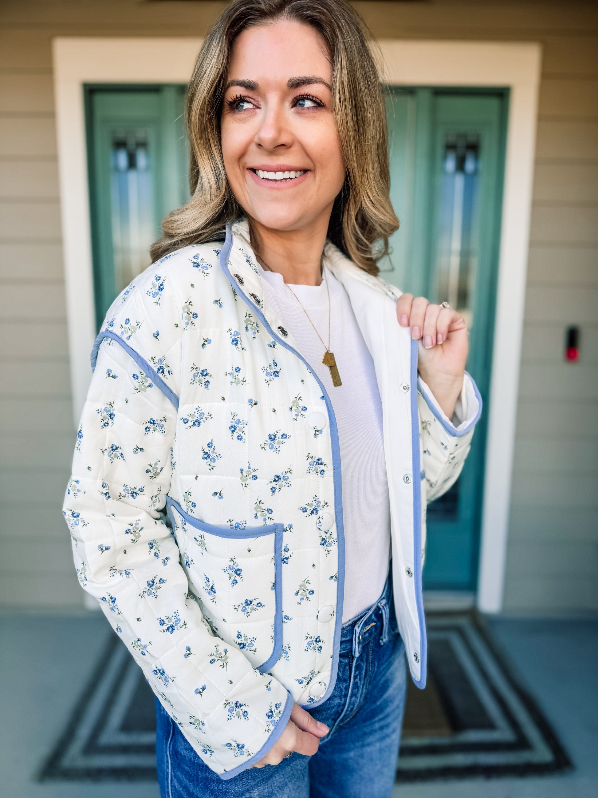 Woman wearing a floral quilted jacket with blue trim in front of a house entrance.Bloom in Blue Quilted Jacket