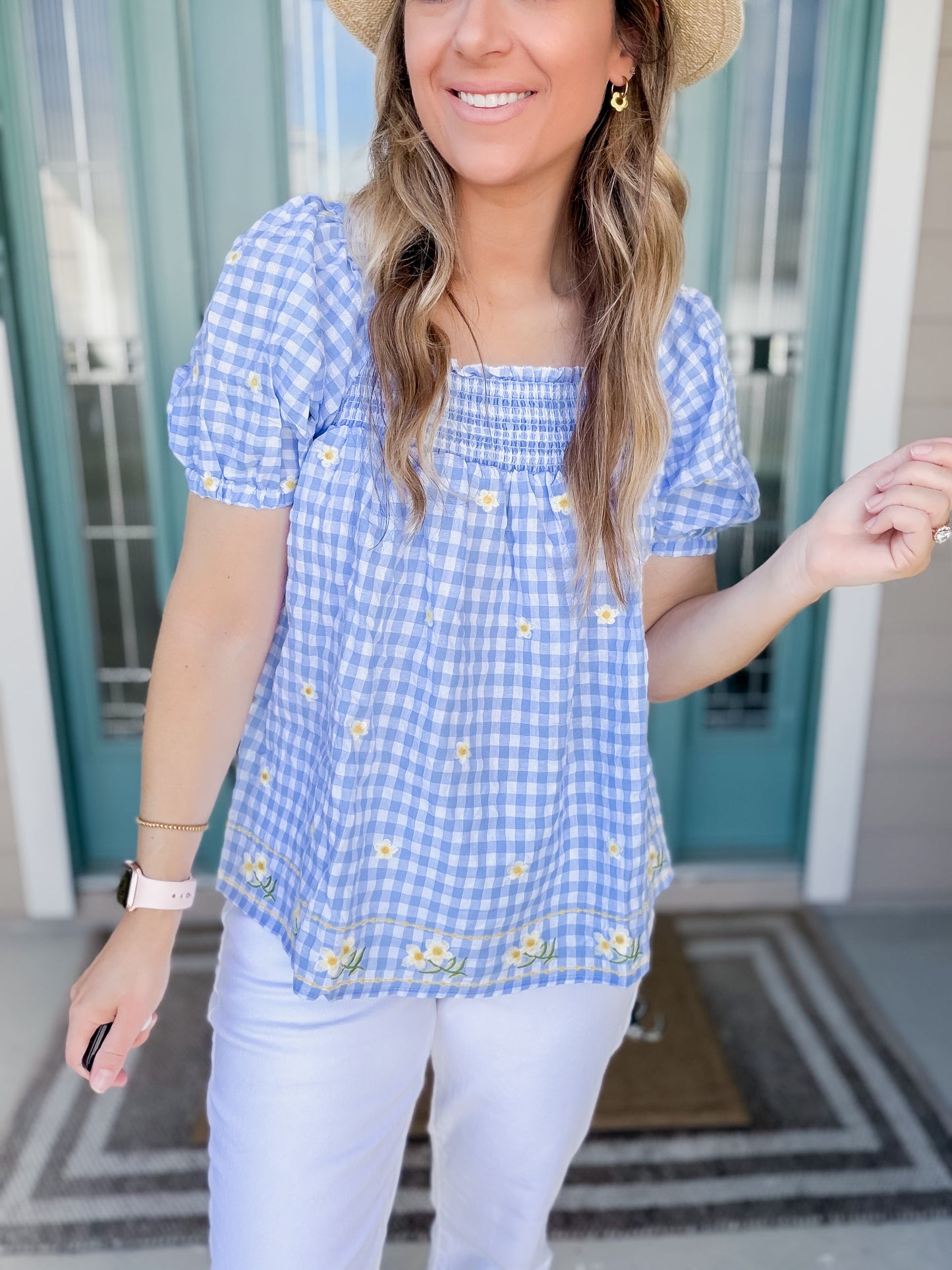 Woman wearing a blue gingham top with yellow flowers embroidered.
