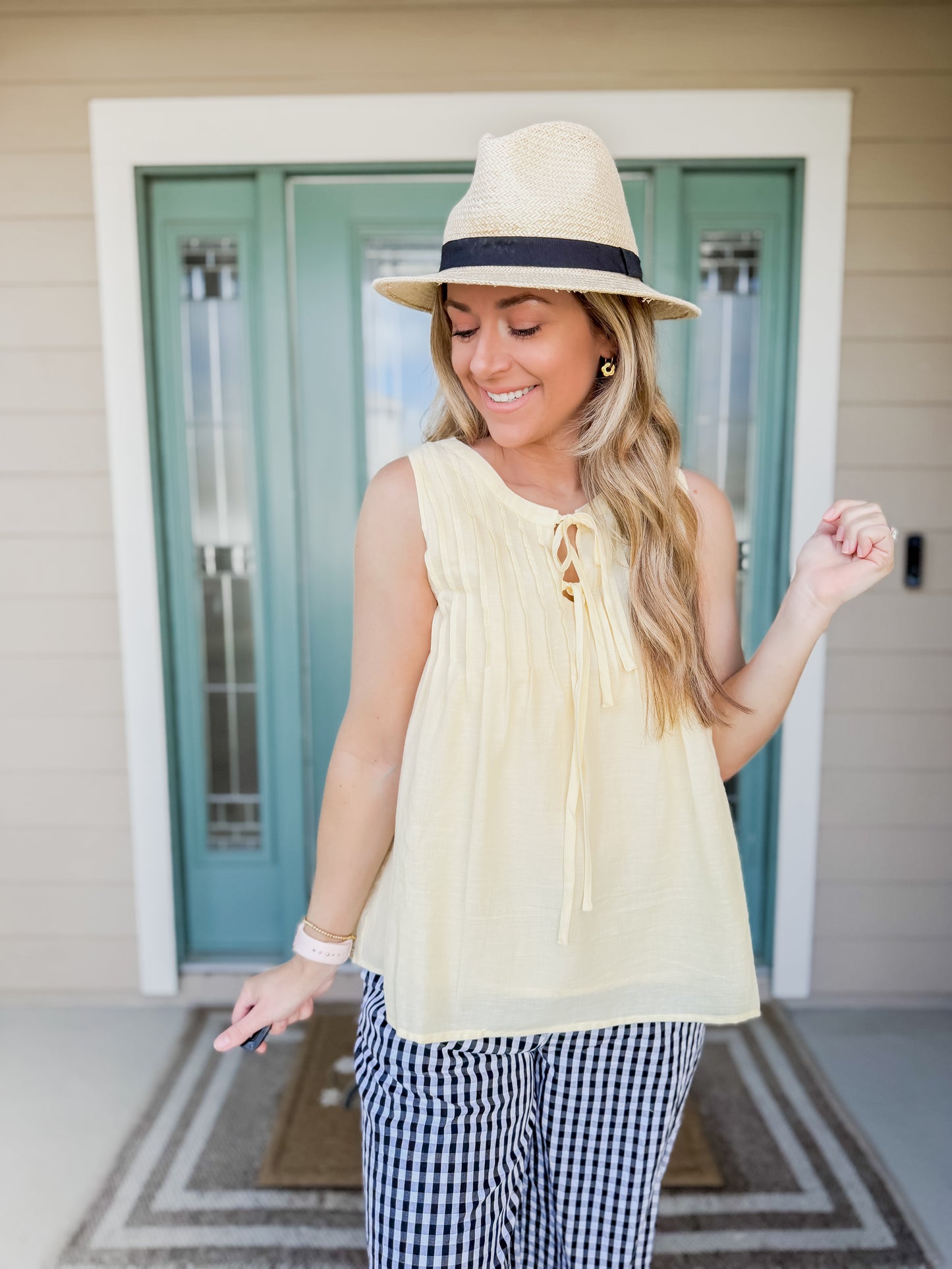 Woman wearing a yellow short sleeve pintuck top and checkered pants on a porch.