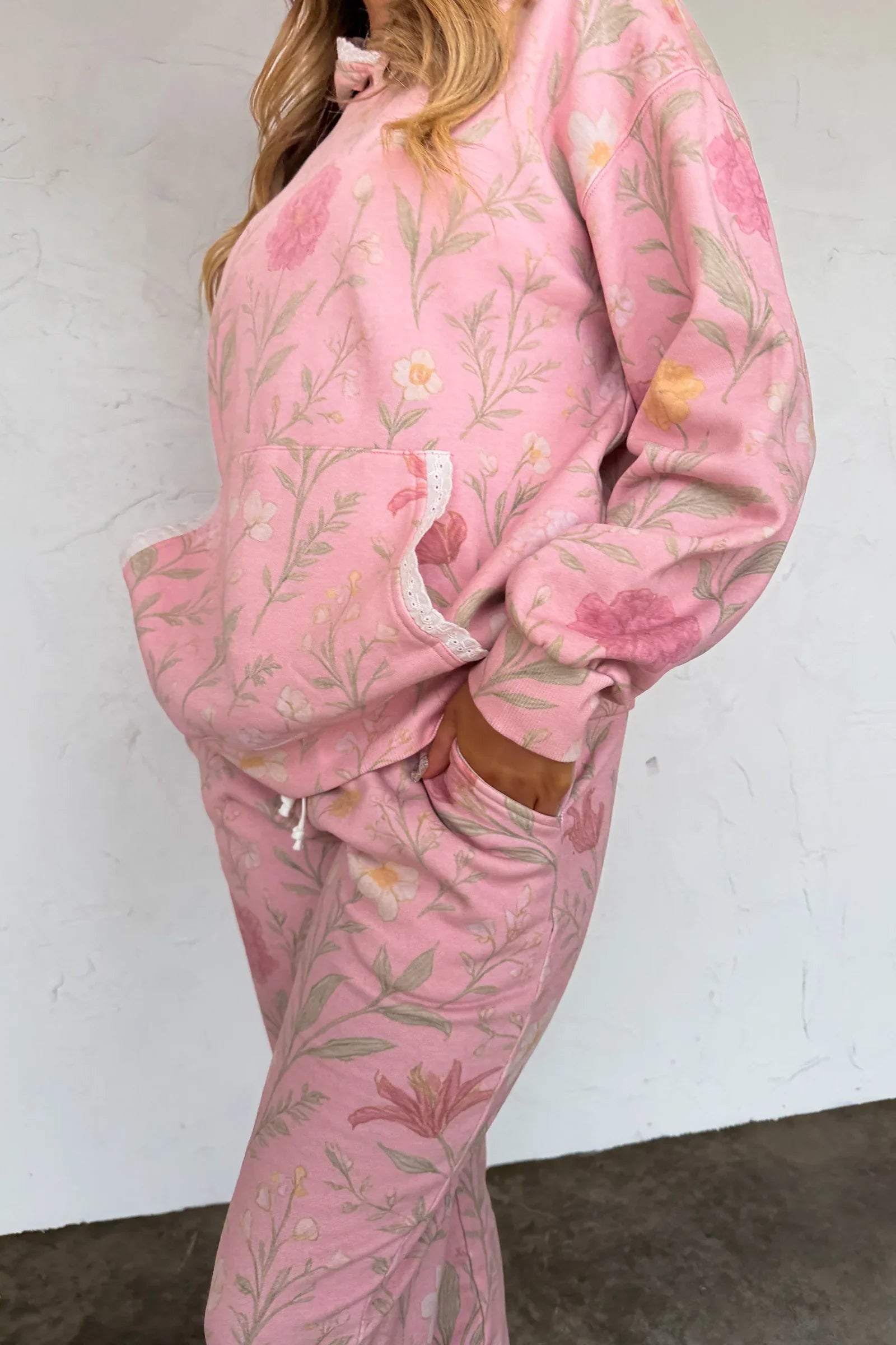 Person wearing a pink floral tracksuit against a white wall.