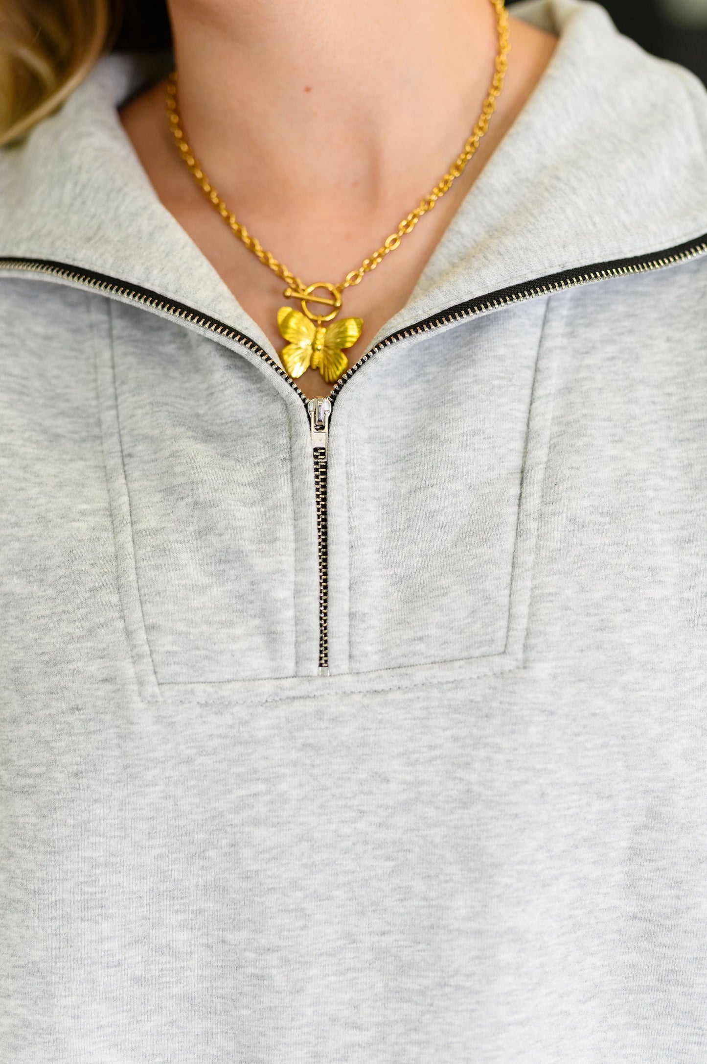 Person wearing a gray zip-up hoodie and gold necklace with a pendant.