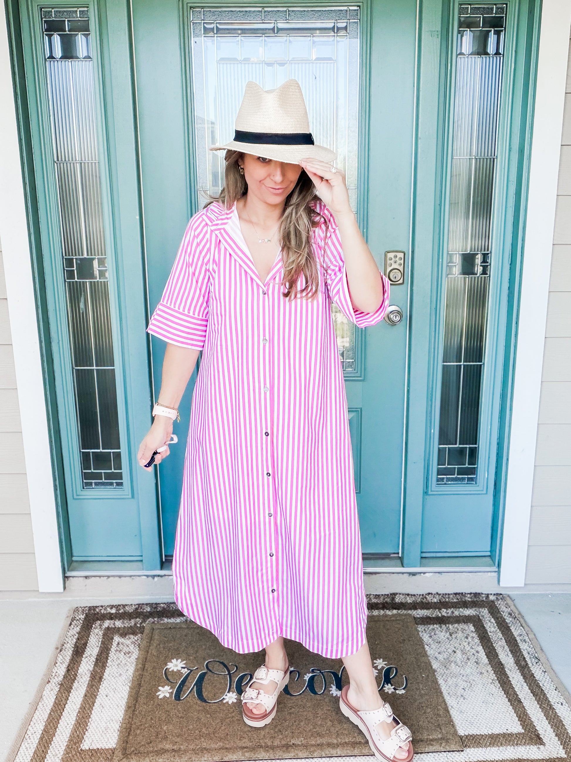 Woman wearing a pink and white striped dress and hat in front of a blue door.