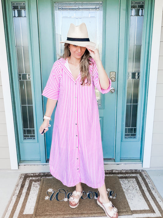 Woman wearing a pink and white striped dress and hat in front of a blue door.