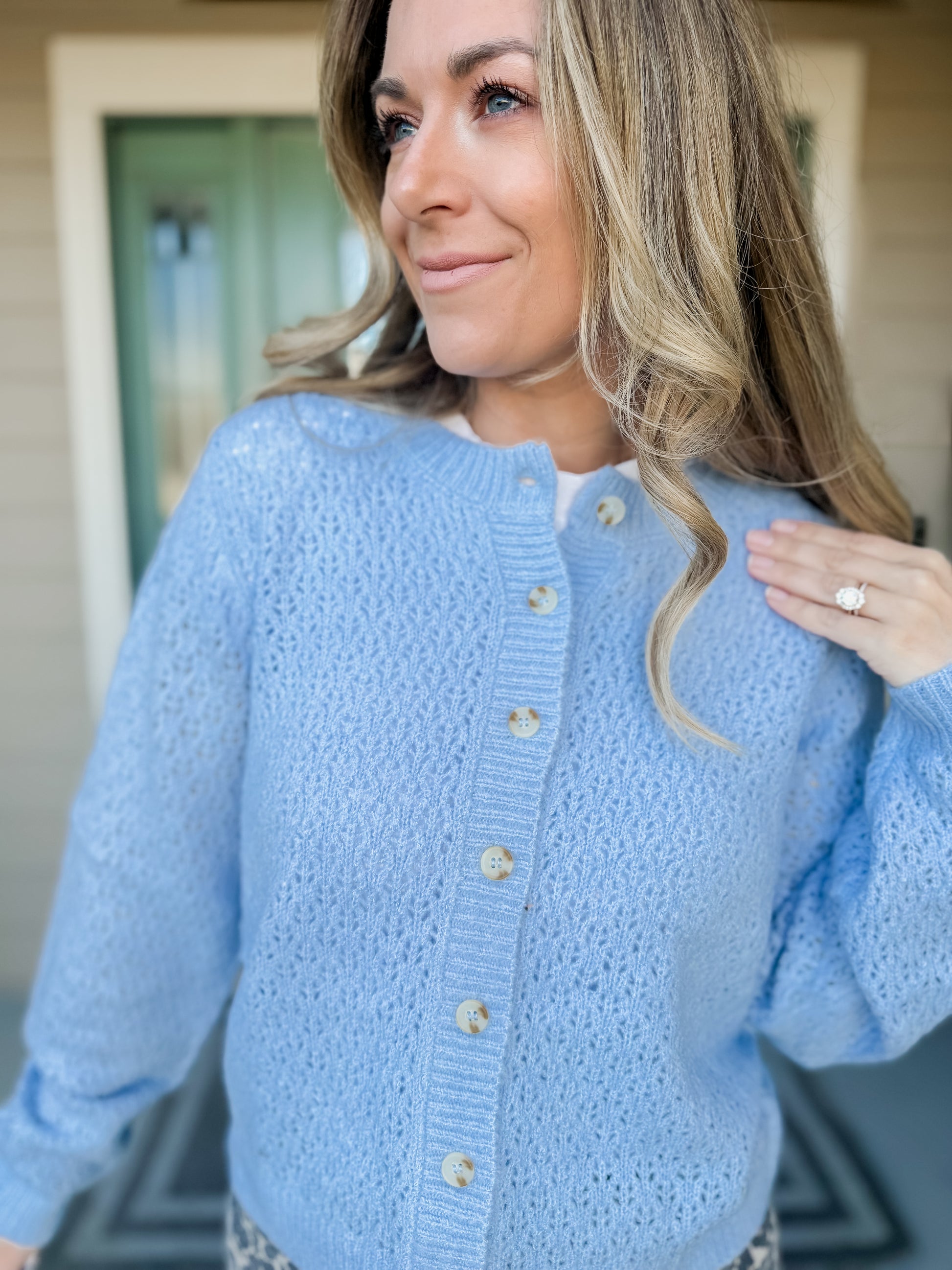 Woman wearing a light blue cardigan with buttons and knit weave design with a neutral background. called haven eyelet knit cardigan. 