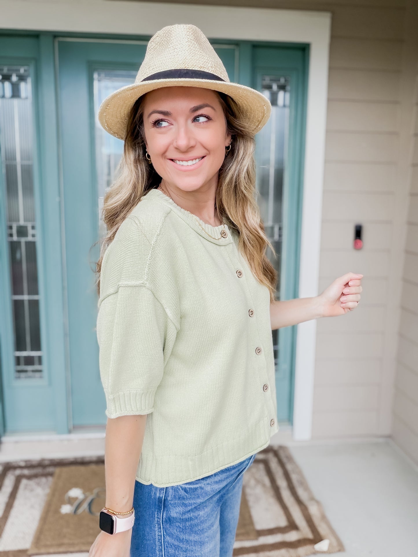 Woman wearing a light green knit sweater top with buttons showing side view of short sleeve detail. 