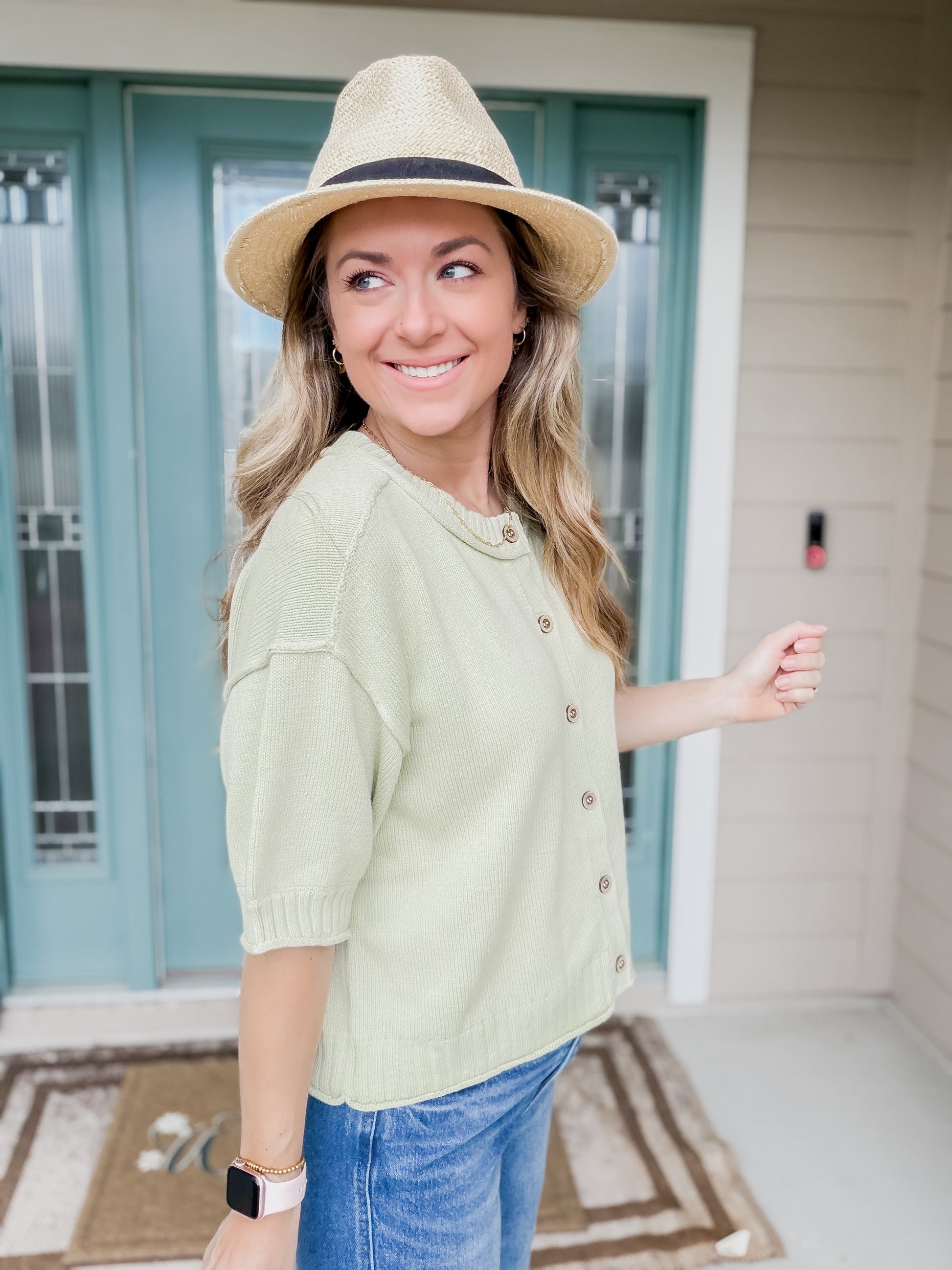 Woman wearing a light green knit sweater top with buttons showing side view of short sleeve detail. 