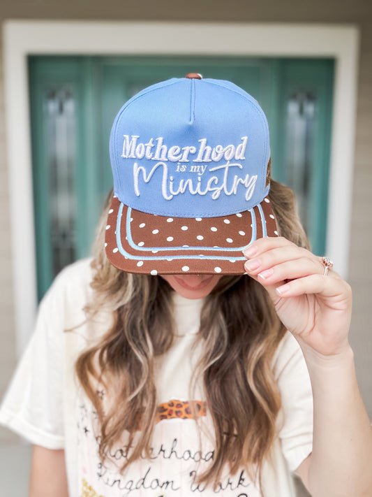Person wearing a blue and brown cap with 'Motherhood is my Ministry' text.