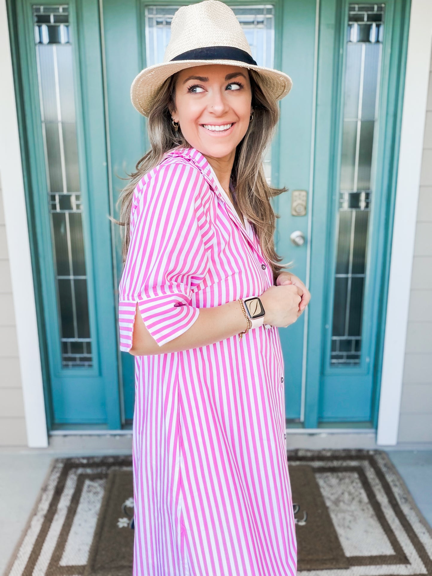 Woman wearing a pink and white striped dress and hat, standing in front of a teal door. side view of sleeves 