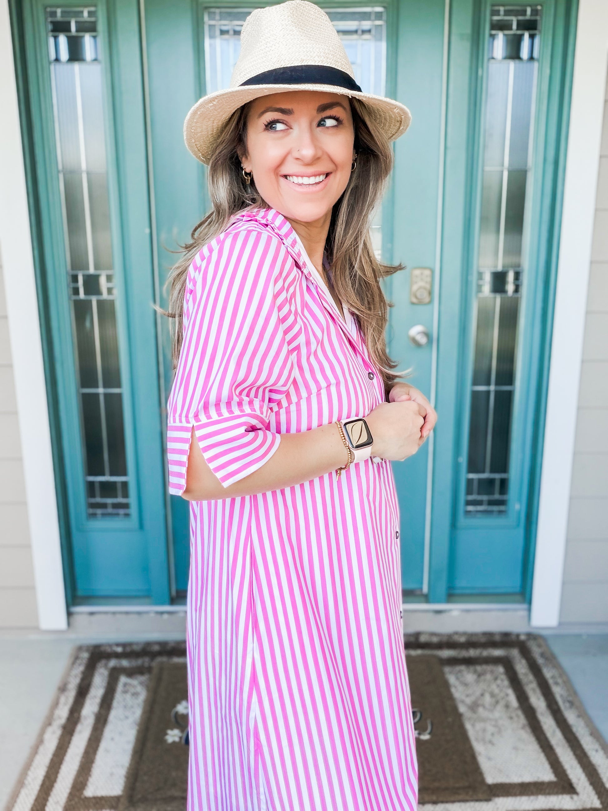 Woman wearing a pink and white striped dress and hat, standing in front of a teal door. side view of sleeves 