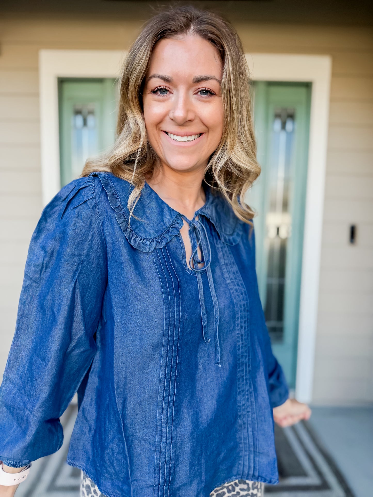 Woman wearing a blue blouse standing in front of a house. called Cerulean collared blouse. 
