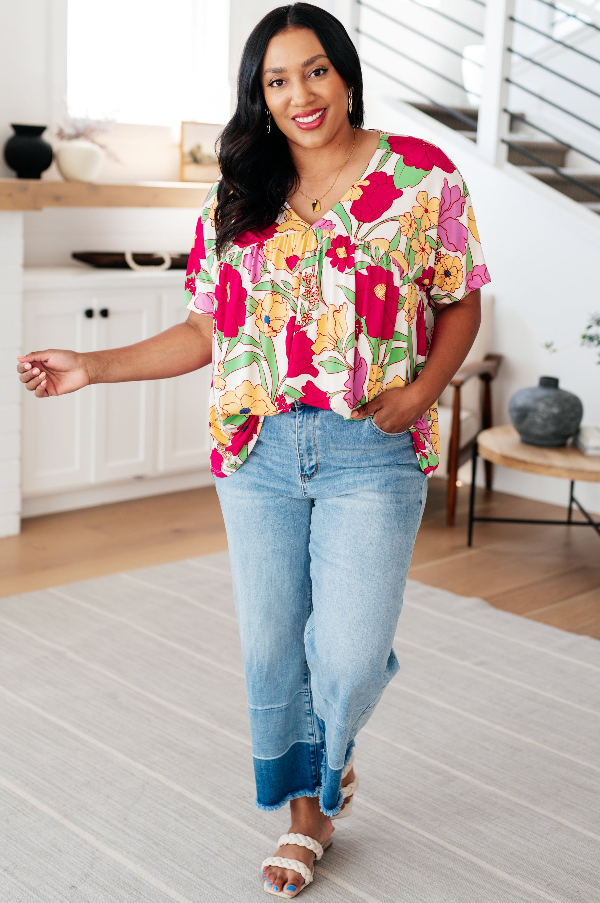 Woman wearing a colorful floral blouse and blue jeans in a home setting