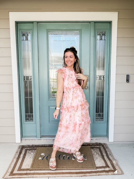 Woman in a pink floral tulle midi dress standing in front of a teal door.