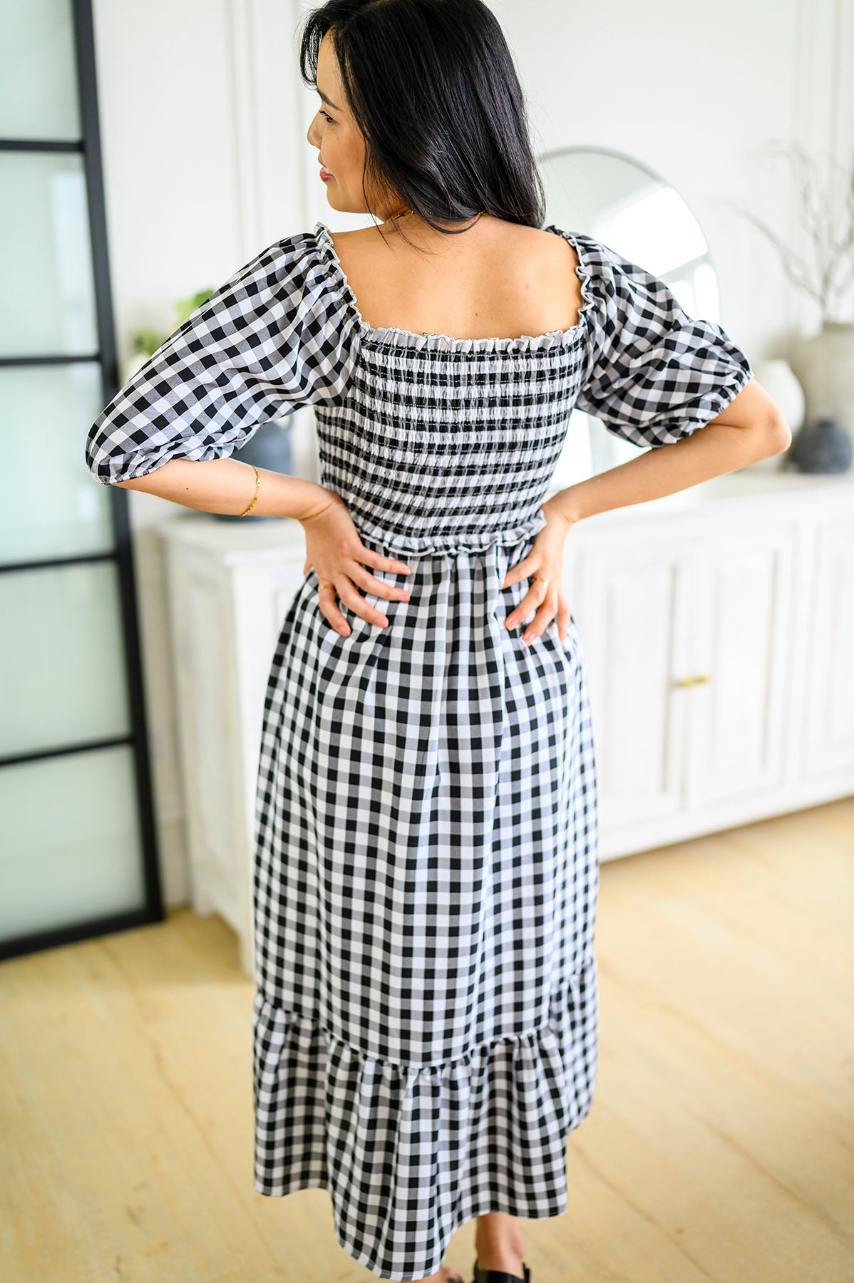 Woman wearing a black and white checkered dress in a room with a white couch and glass door.