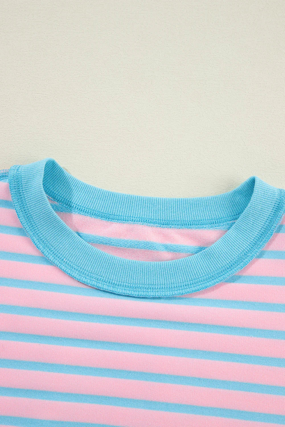 Close-up of a pink and blue striped shirt with a blue collar on a beige background