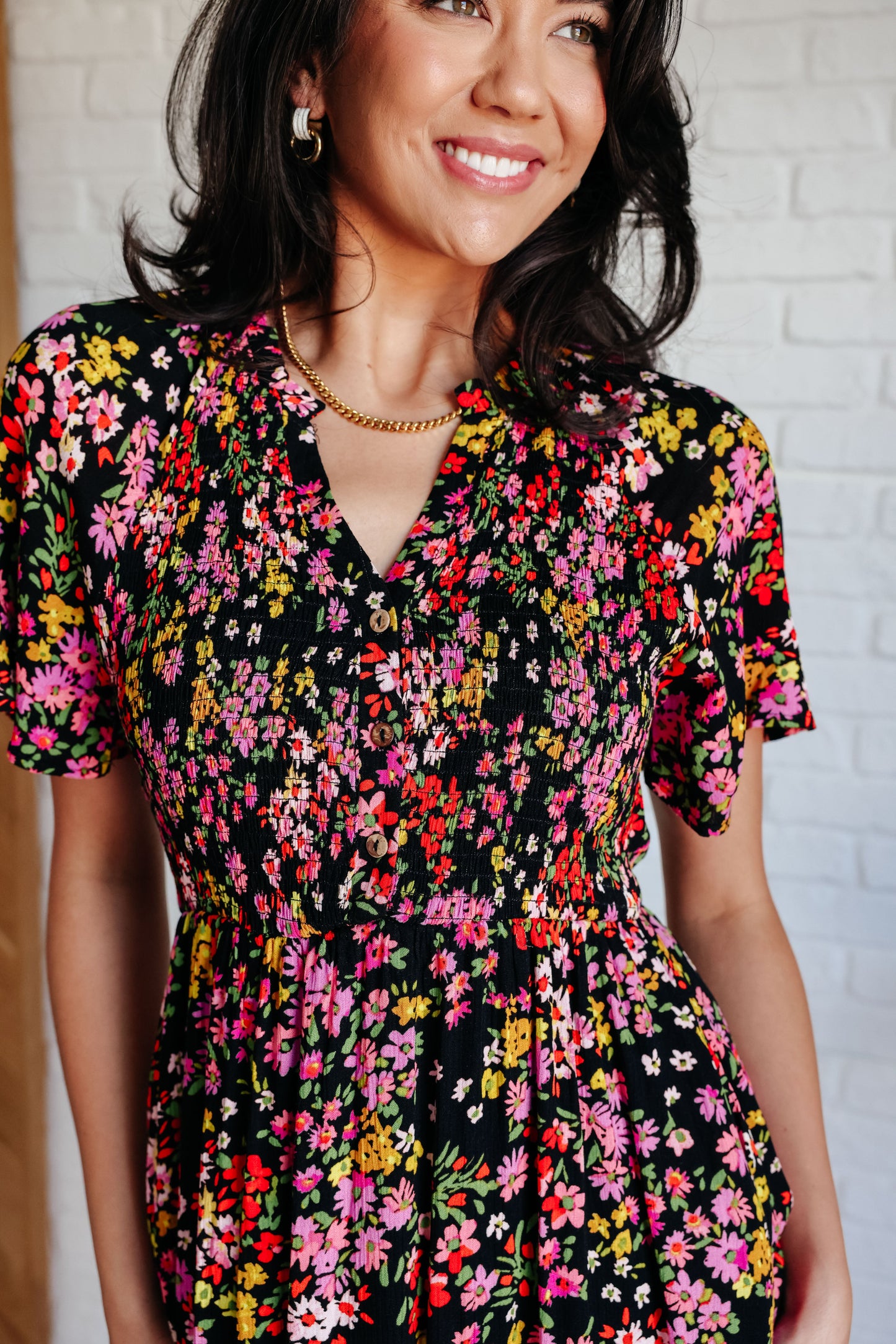 Woman wearing a floral dress against a white brick wall.